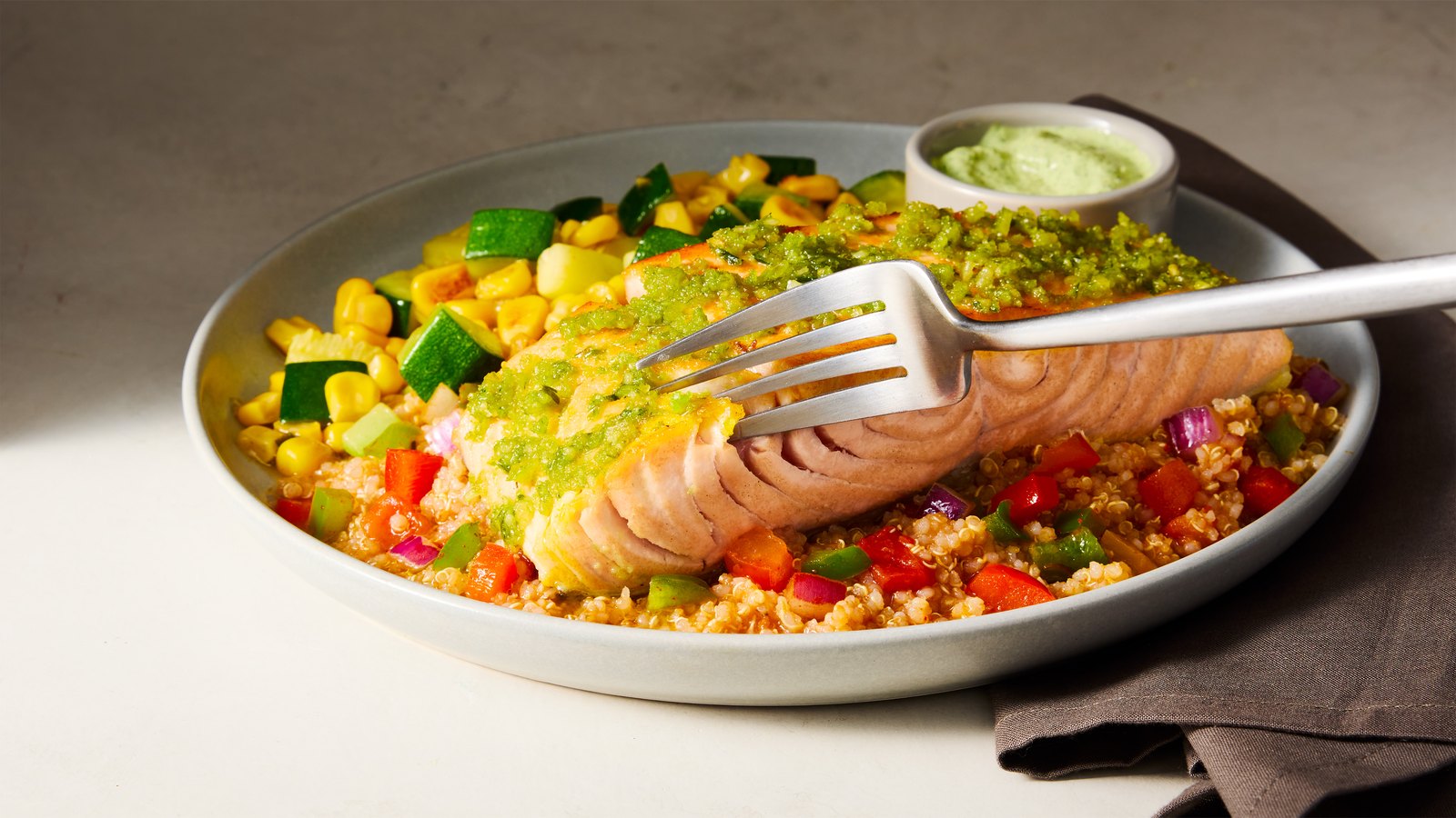 A Factor salmon fillet with pesto over quinoa, corn and peppers, a fork lifting a bite