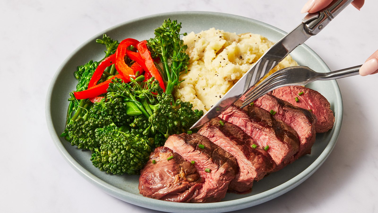 A Factor steak sliced on a plate with mashed potato and broccolini