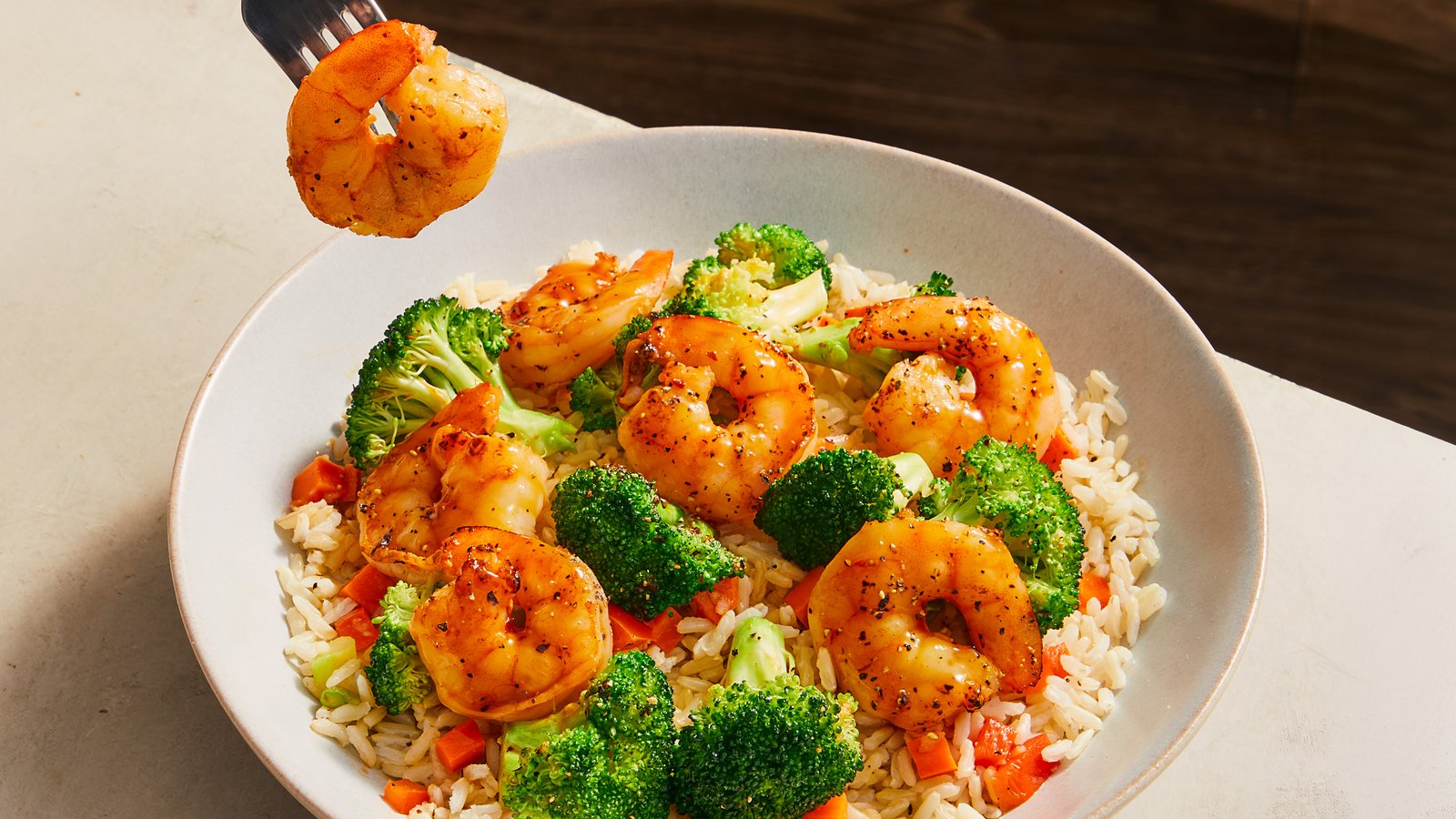 A bowl of Factor shrimp and broccoli over rice, a fork lifting one shrimp